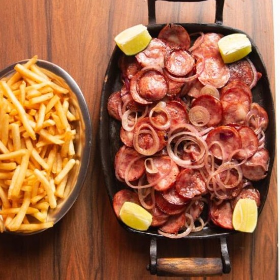 Travessa de calabresa com rodelas de cebola e limão, acompanhada por batatas fritas